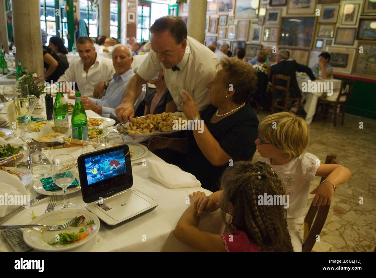 Kinder, die mit Erwachsenen beim Essen Computerfilme anschauen. Innenrestaurant Trattoria da Romano Insel Burano. HOMER SYKES aus den 2000er Jahren in Venedig Stockfoto