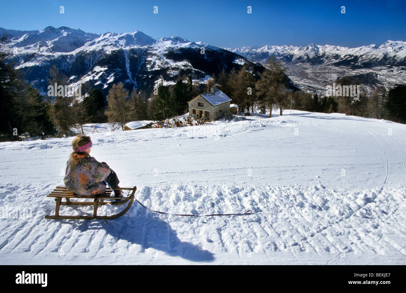 Kind auf Schlitten mit Blick auf die Berge am Cabane l'Illhorn, Wallis, Schweiz Stockfoto