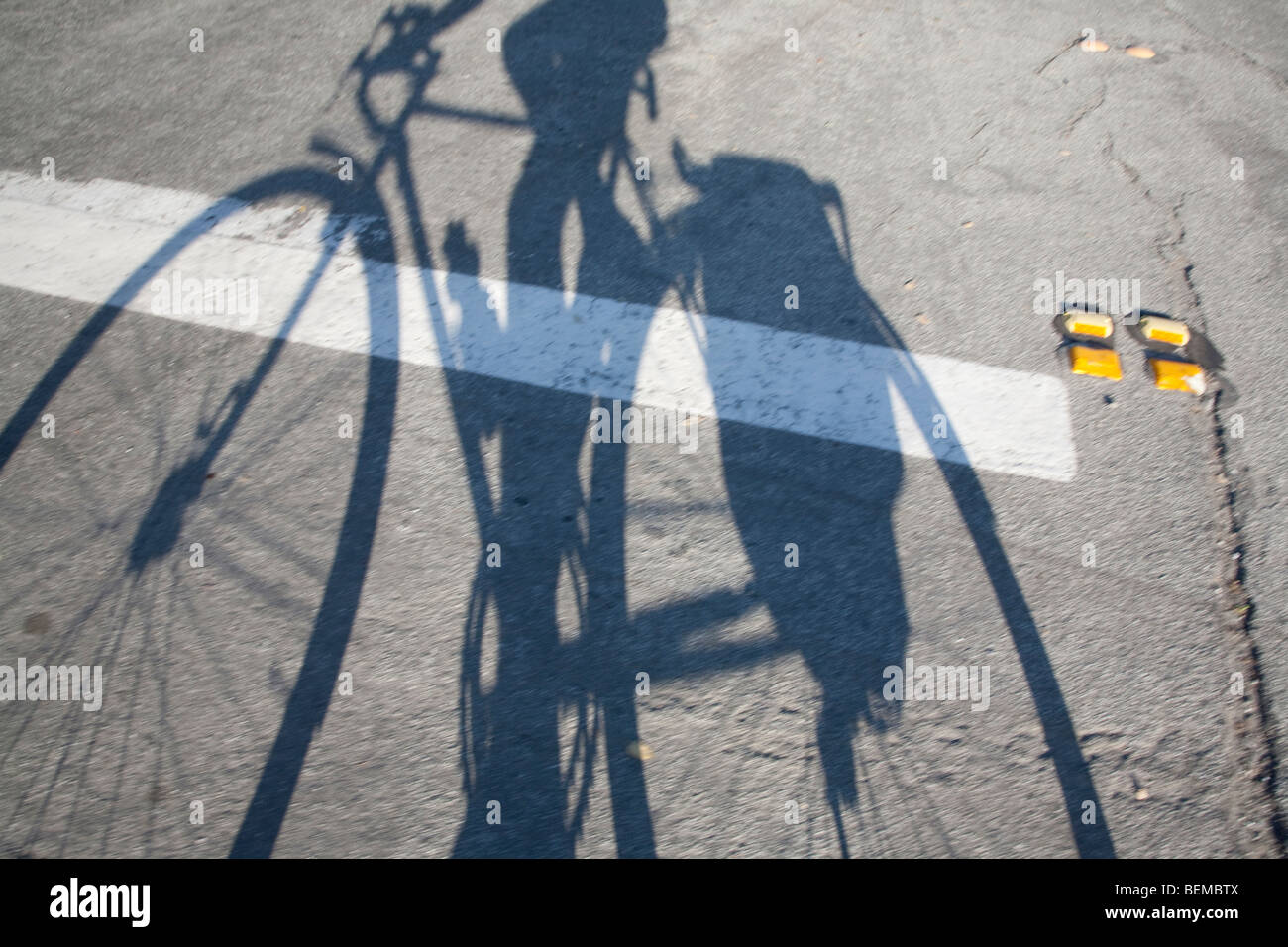 Des Radfahrers langen Schatten auf die Straße fallen. Die Radfahrer trägt Ausrüstung im Koffer neben das Hinterrad. Stockfoto