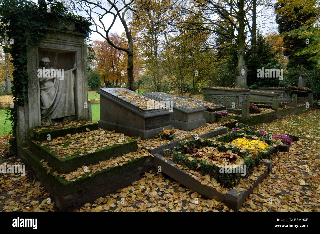 Blumen auf alten Grabsteinen bedeckt im Herbstlaub am Friedhof im November Stockfoto