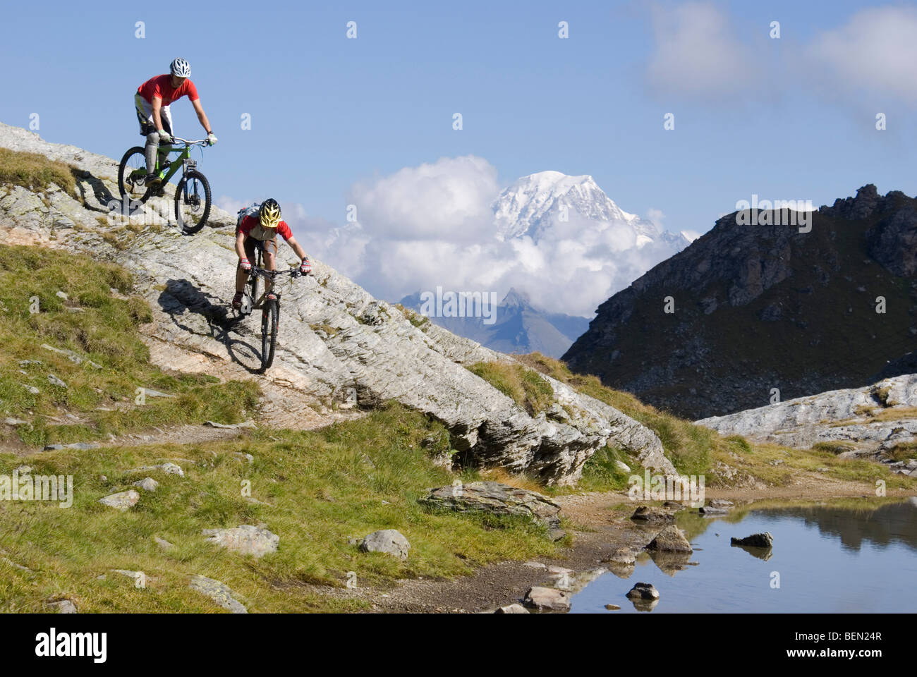 Zwei Mountainbiker fahren einen felsigen Hang an einem See in den Bergen in der Nähe von Les Arcs in den französischen Alpen. Stockfoto