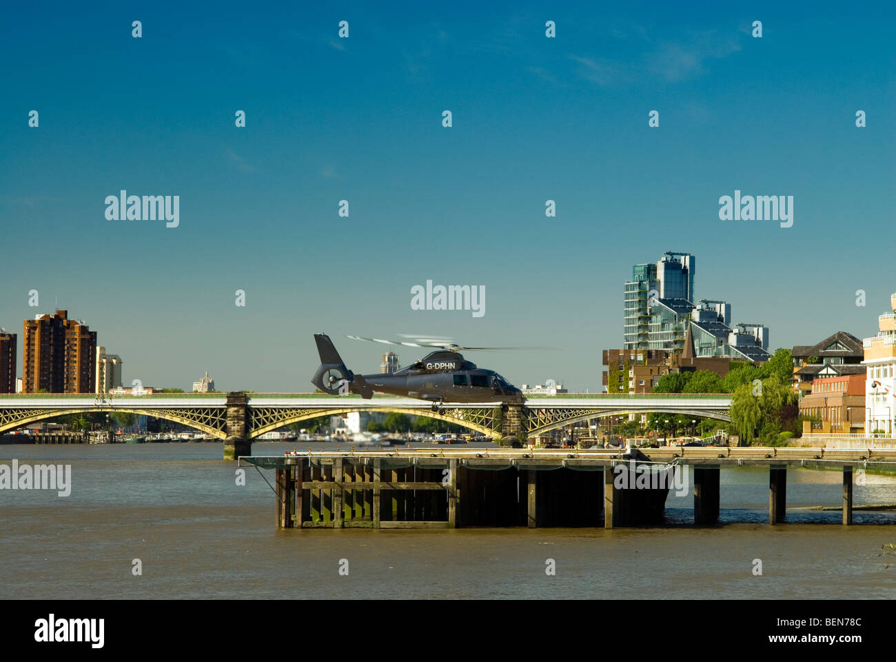 Battersea Hubschrauberlandeplatz mit einem Helikopter abheben und Battersea Brücke im Hintergrund an einem perfekten Tag Stockfoto