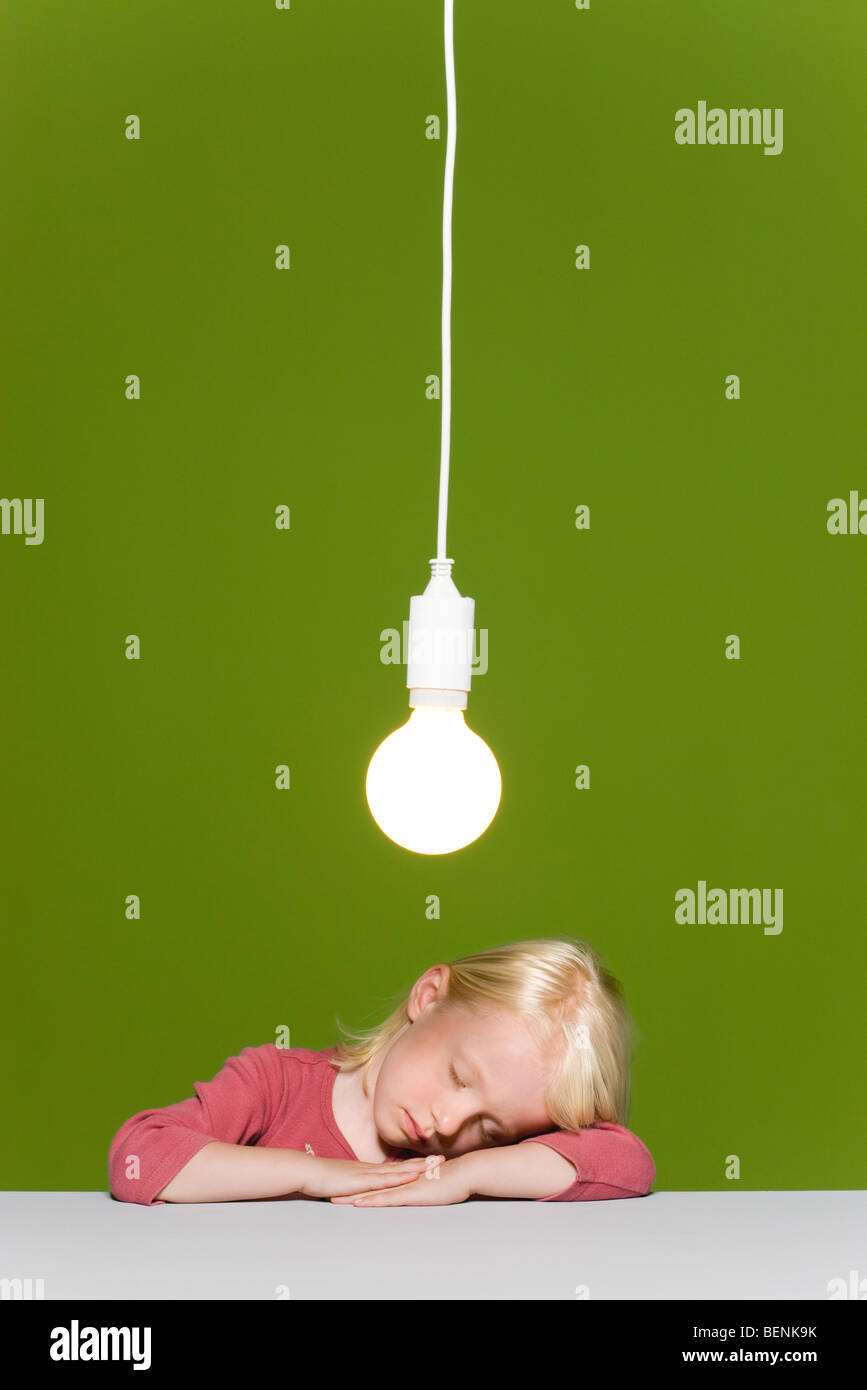 Kleines Mädchen schlafen ruhen Kopf an Armen, leuchtende Glühbirne über Kopf ausgesetzt Stockfoto