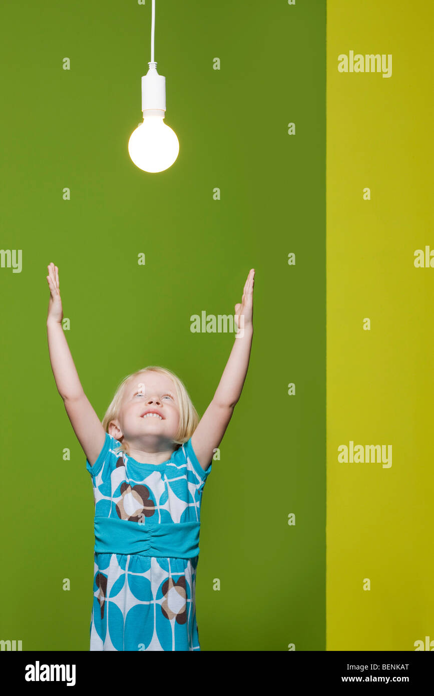 Kleines Mädchen mit erhobenen Armen, Overhead ausgesetzt für Glühbirne zu erreichen Stockfoto