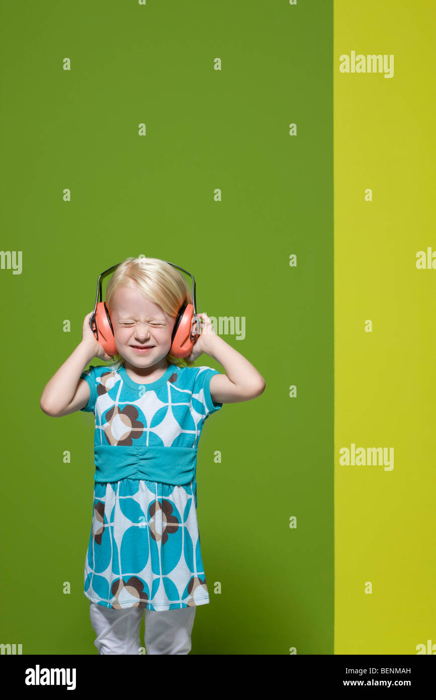 Kleines Mädchen mit Augen geschlossen tragen schützende Kopfhörer Stockfoto