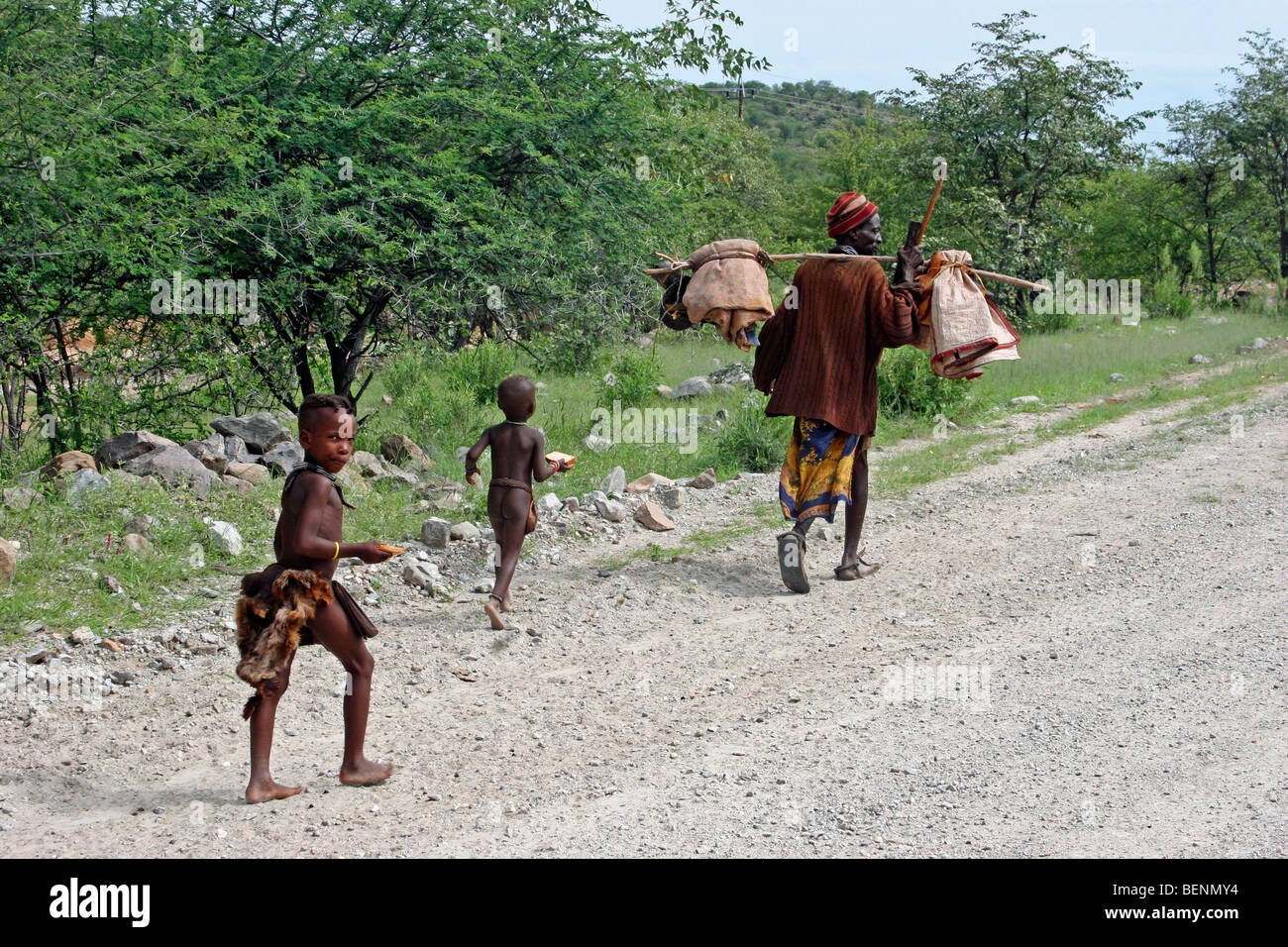 Himba Stamm Kinder und Mann trägt merchandise Kiesweg, Kaokoland / Kaokoveld, Kunene Region, Namibia, Südafrika Stockfoto