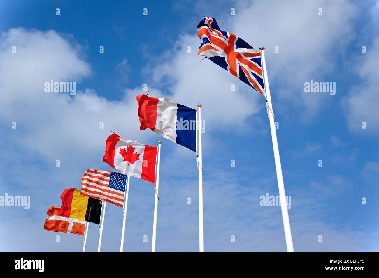 Nationalflaggen auf Fahnenmasten fliegen im Wind gegen bewölktem Himmel Stockfoto