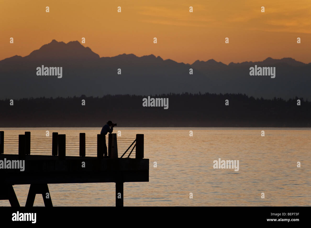 Fotograf auf Alki Beach in West Seattle, Washington. Die Sonne geht über die Olympic Mountains und Bainbridge Island. Stockfoto