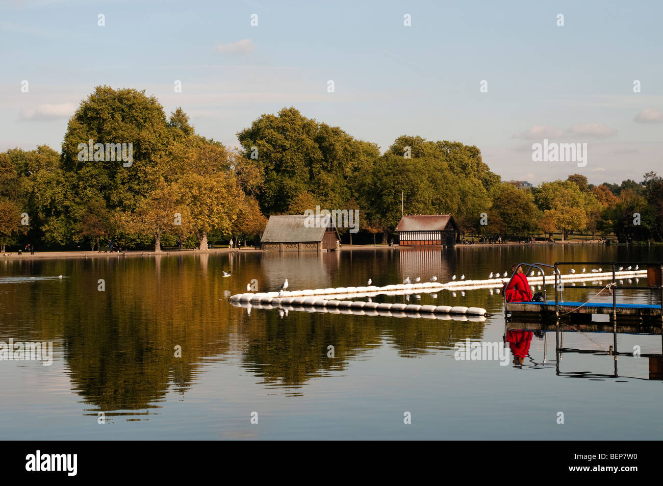 Frau im roten Mantel sitzt an einem Anlegesteg am Serpentine Lake, Hyde Park, London, Westminster, SW1 Stockfoto