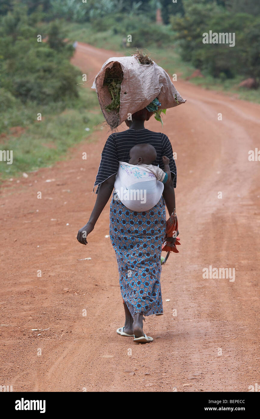 UGANDA-Frau mit baby und laden auf den Kopf, während sie entlang der Straße, Kayunga Bezirk geht. Foto: SEAN SPRAGUE Stockfoto