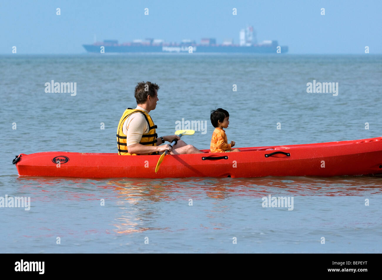 Mann im Kajak mit Kind und Containerschiff in der Nordsee Stockfoto