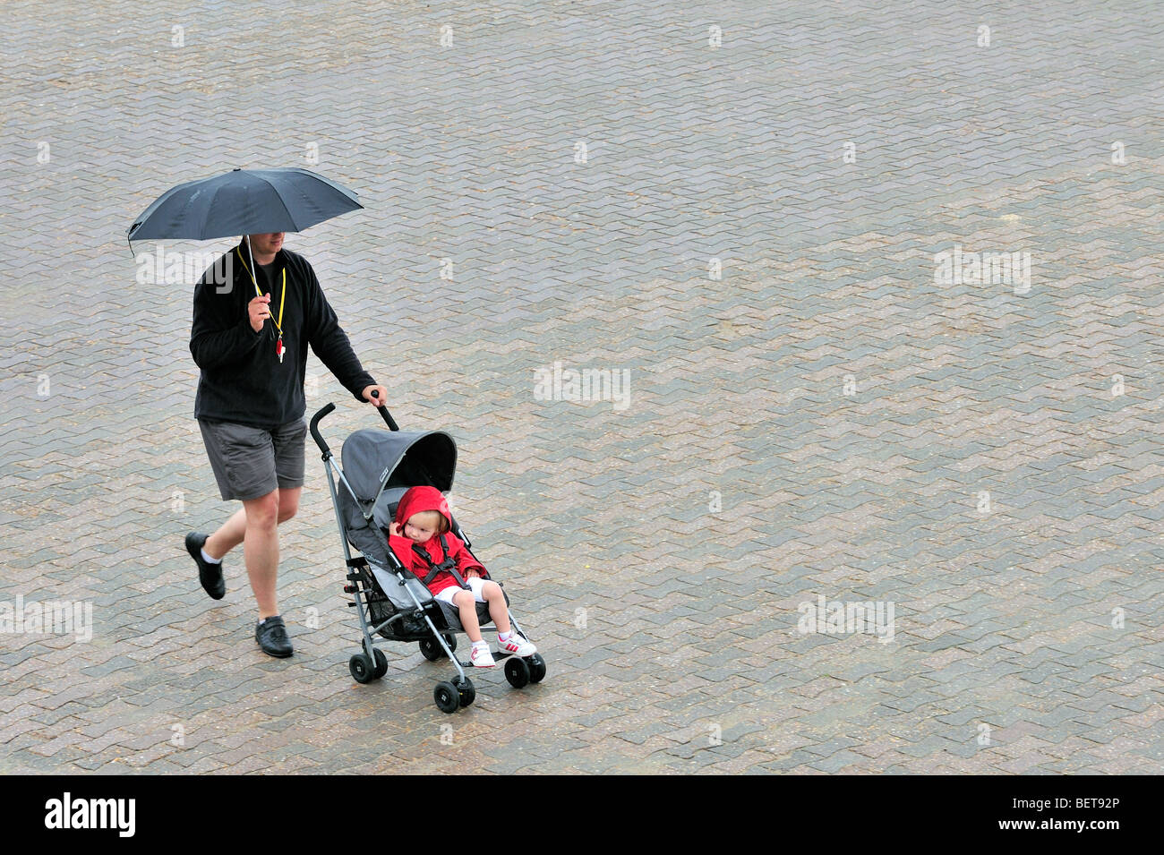 Papa mit Sonnenschirm und Baby im Kinderwagen zu Fuß über die Promenade entlang der Küste am Badeort an regnerischen Tag in den Sommerferien Stockfoto