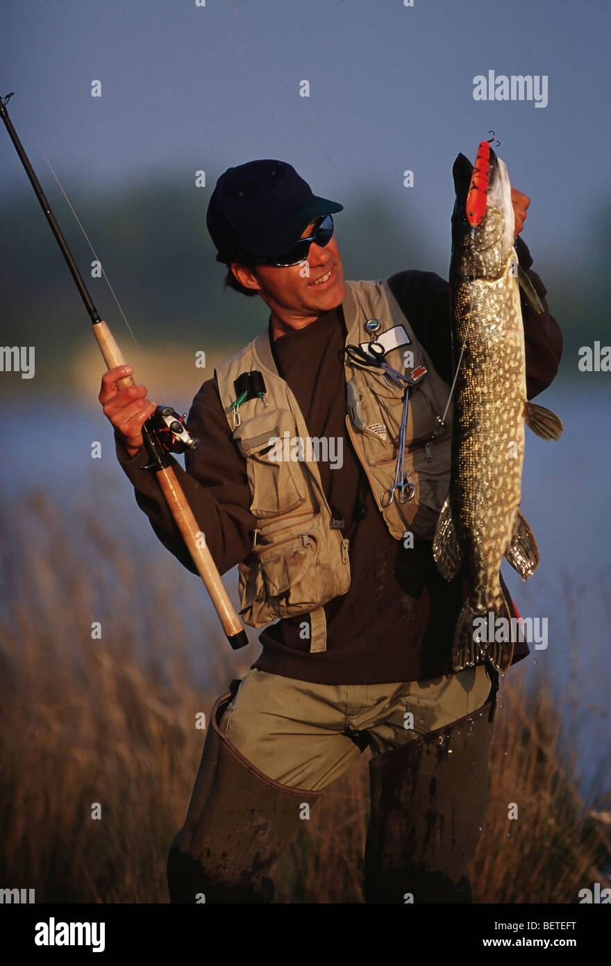 Angler hält einen Stab und einen Fisch. Stockfoto