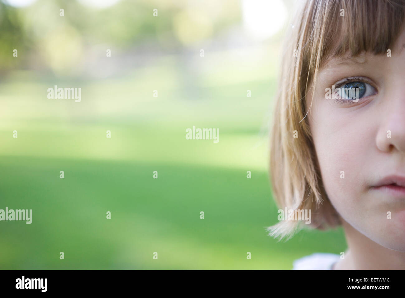 sieben Jahre altes Mädchen Blick in die Kamera mit ernsten Ausdruck, grüner Hintergrund, im Freien, Nahaufnahme des Gesichts Stockfoto