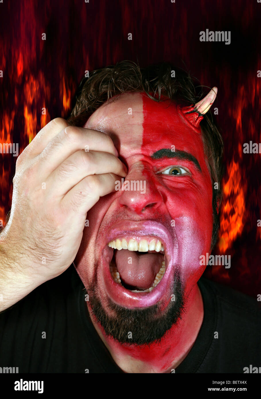 Halb Teufel Monster Mann angegriffen von einer Hand sein Auge ausstechen. Feuer Flammen im Hintergrund. Stockfoto