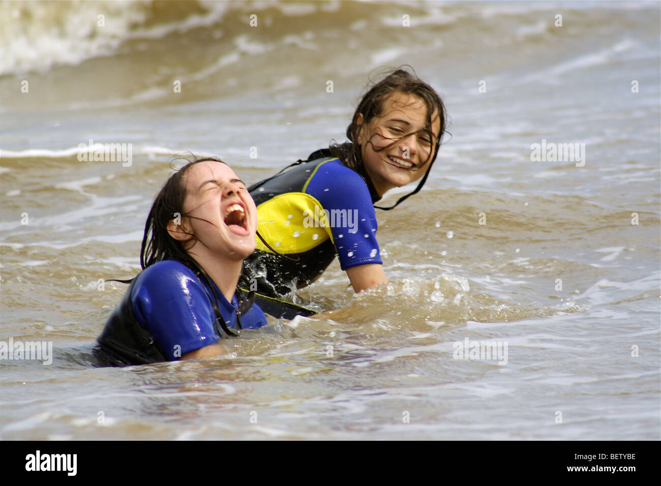 zwei Mädchen, die Schwimmen im Meer in Neoprenanzüge eine großartige Zeit spielen in den Wellen Stockfoto