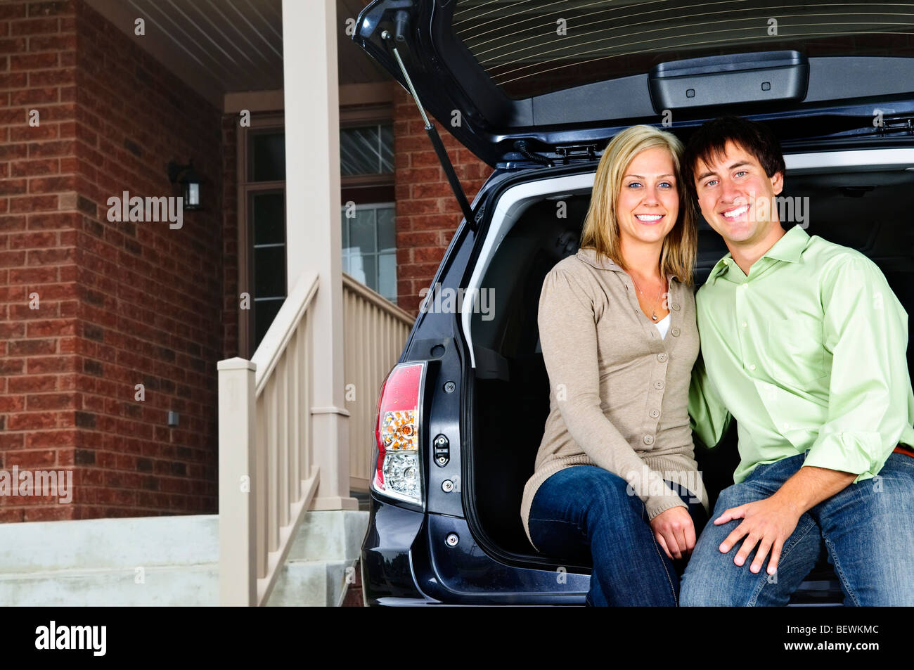 Glückliches junges Paar sitzt an Rückseite Auto auf Auffahrt Stockfoto
