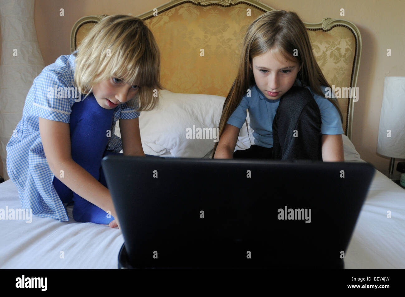 Zwei Mädchen in Schuluniform, mit einem Laptop-Computer auf ihren Eltern-Bett Stockfoto