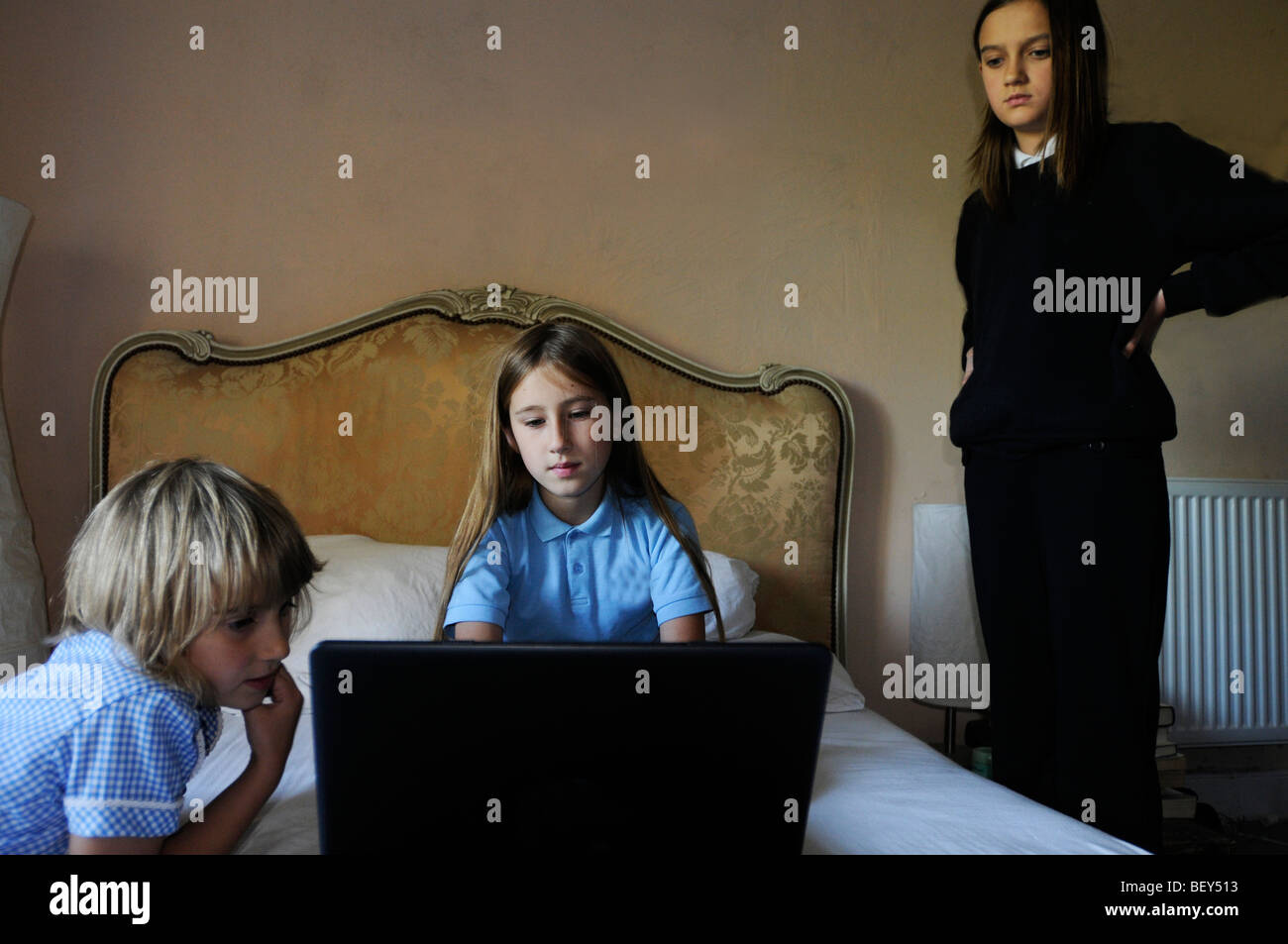 Drei Mädchen in Schuluniform mit einem Laptop auf dem Bett der Eltern ein Mädchen unglücklich aussieht. Stockfoto