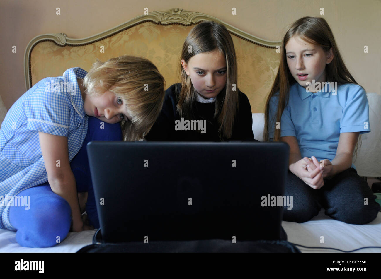 Drei Mädchen in Schuluniform, mit einem Laptop-Computer auf ihren Eltern-Bett Stockfoto