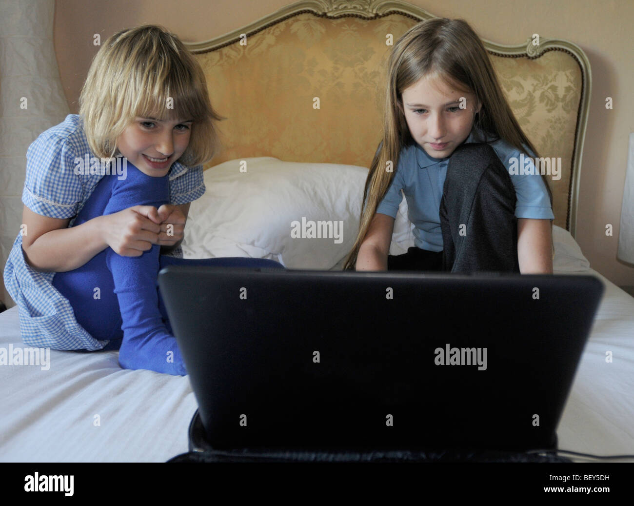 Zwei Mädchen in Schuluniform, mit einem Laptop-Computer auf ihren Eltern-Bett Stockfoto