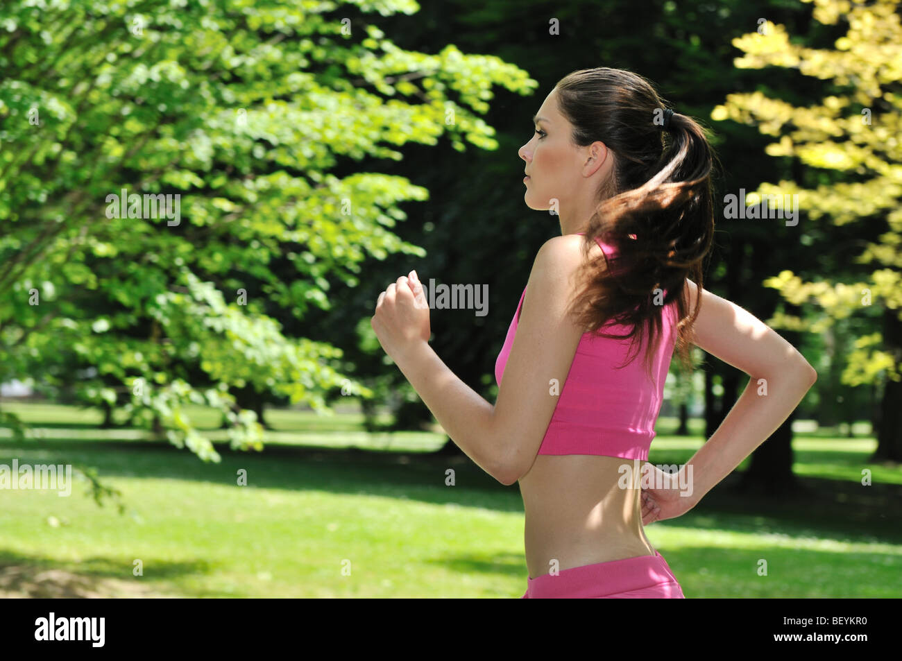 Junge schöne Frau in rosa laufen (Joggen) draußen im Park am sonnigen Tag Stockfoto