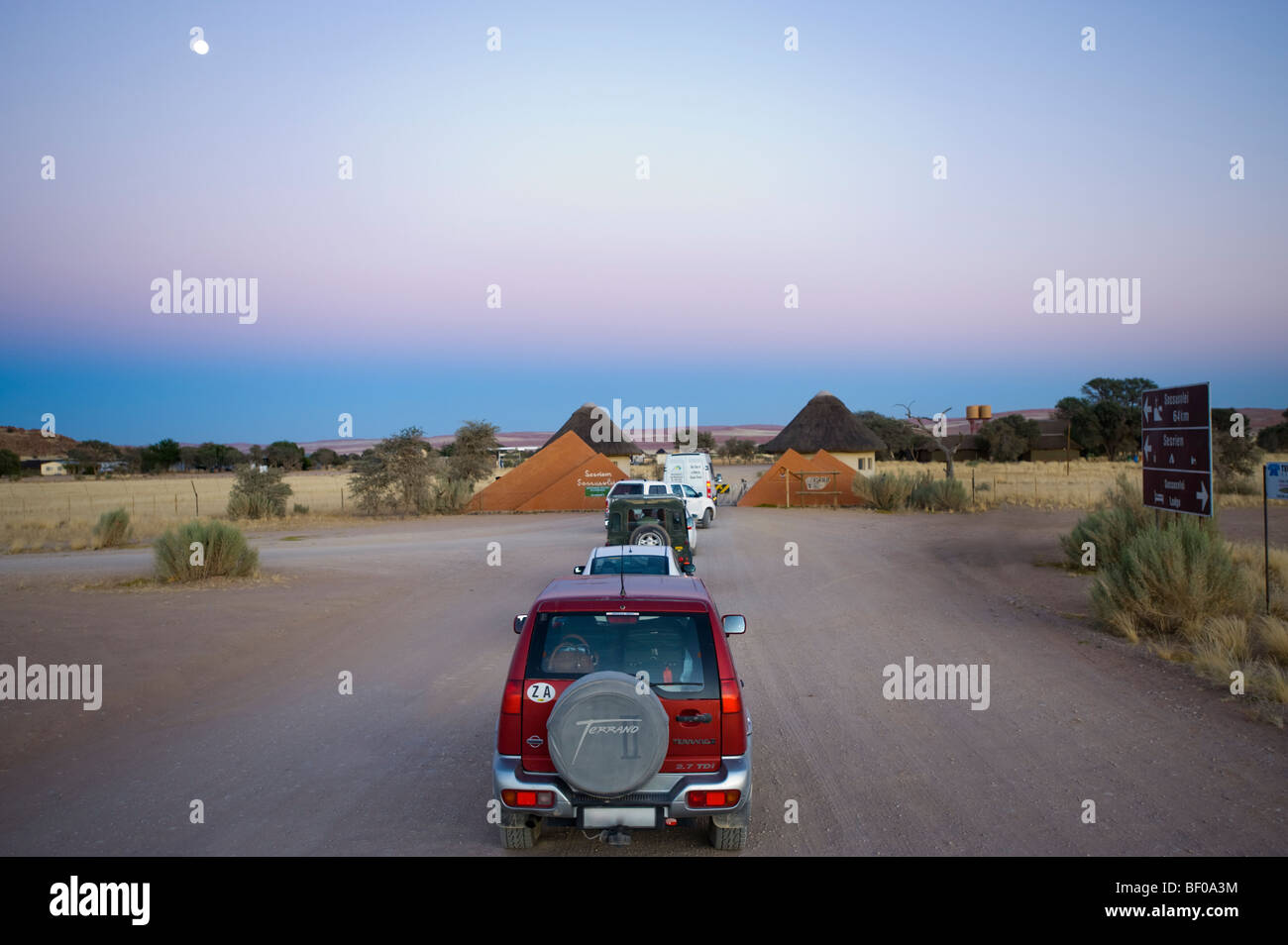 Autos warten am Sesriem Tor öffnen NAMIBIA Wüste SOSSUSVLEI am frühen Morgen Straße Dünen gelb rot orange Sand Staub jeep Stockfoto