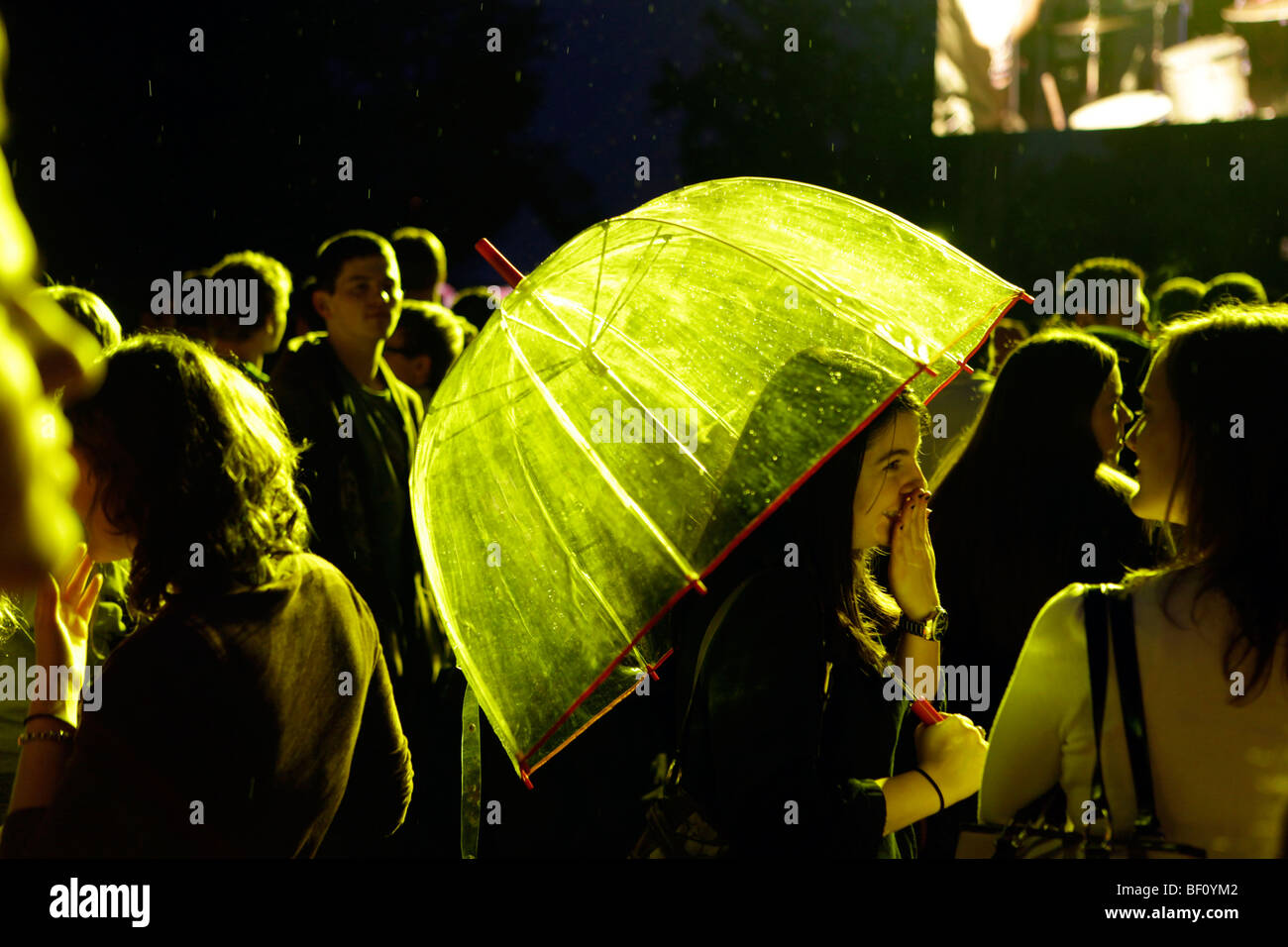 Eine Frau bleibt trocken unter und Regenschirm bei einem Nacht-Musik-Konzert. Stockfoto