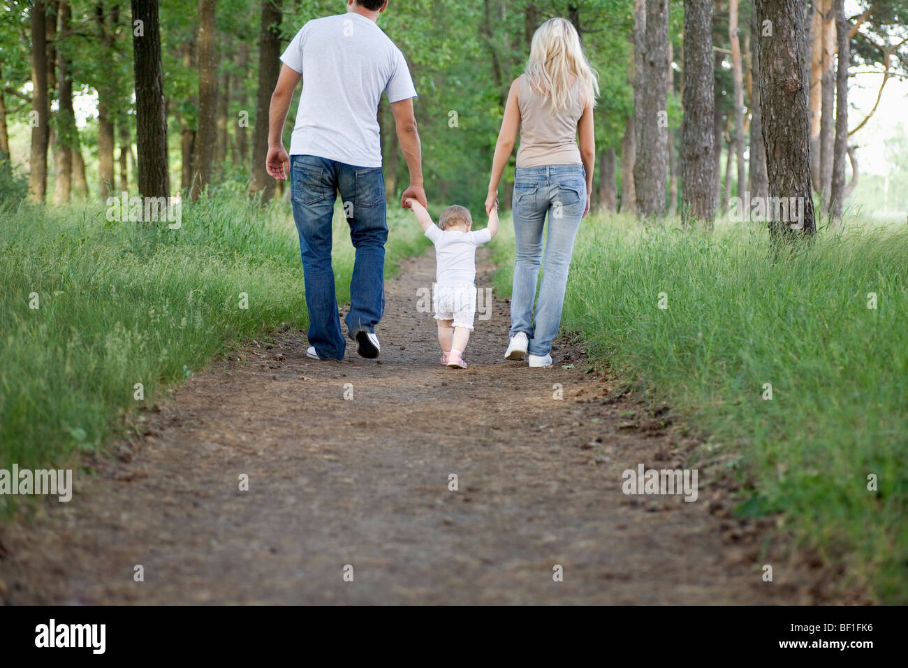 Zwei Eltern, die zu Fuß über einen Waldweg mit ihrer jungen Tochter Stockfoto