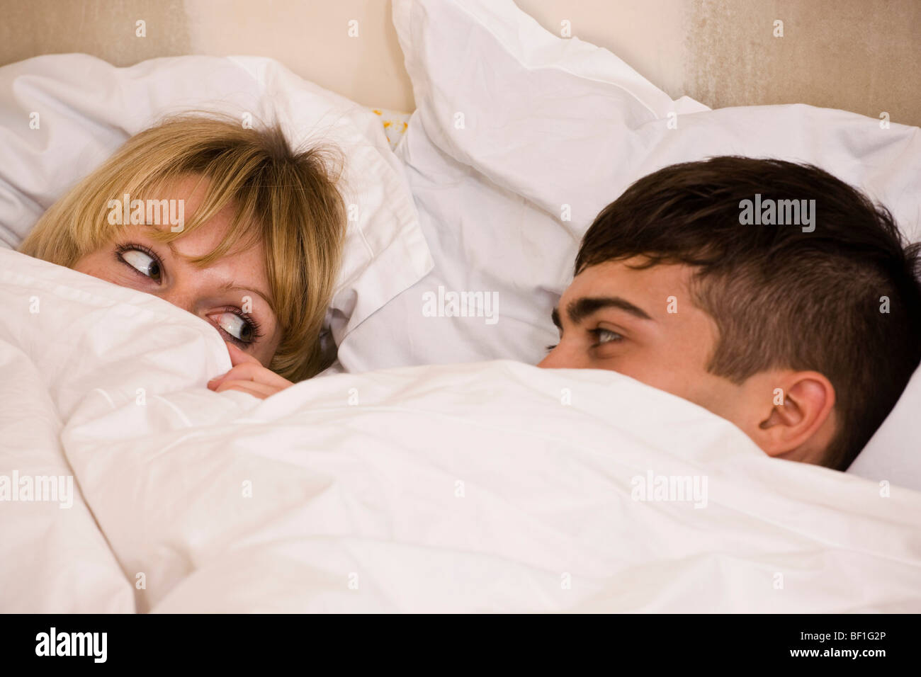 Ein junges Paar im Bett mit der Bettdecke vorfuhren, um ihre Augen Stockfoto