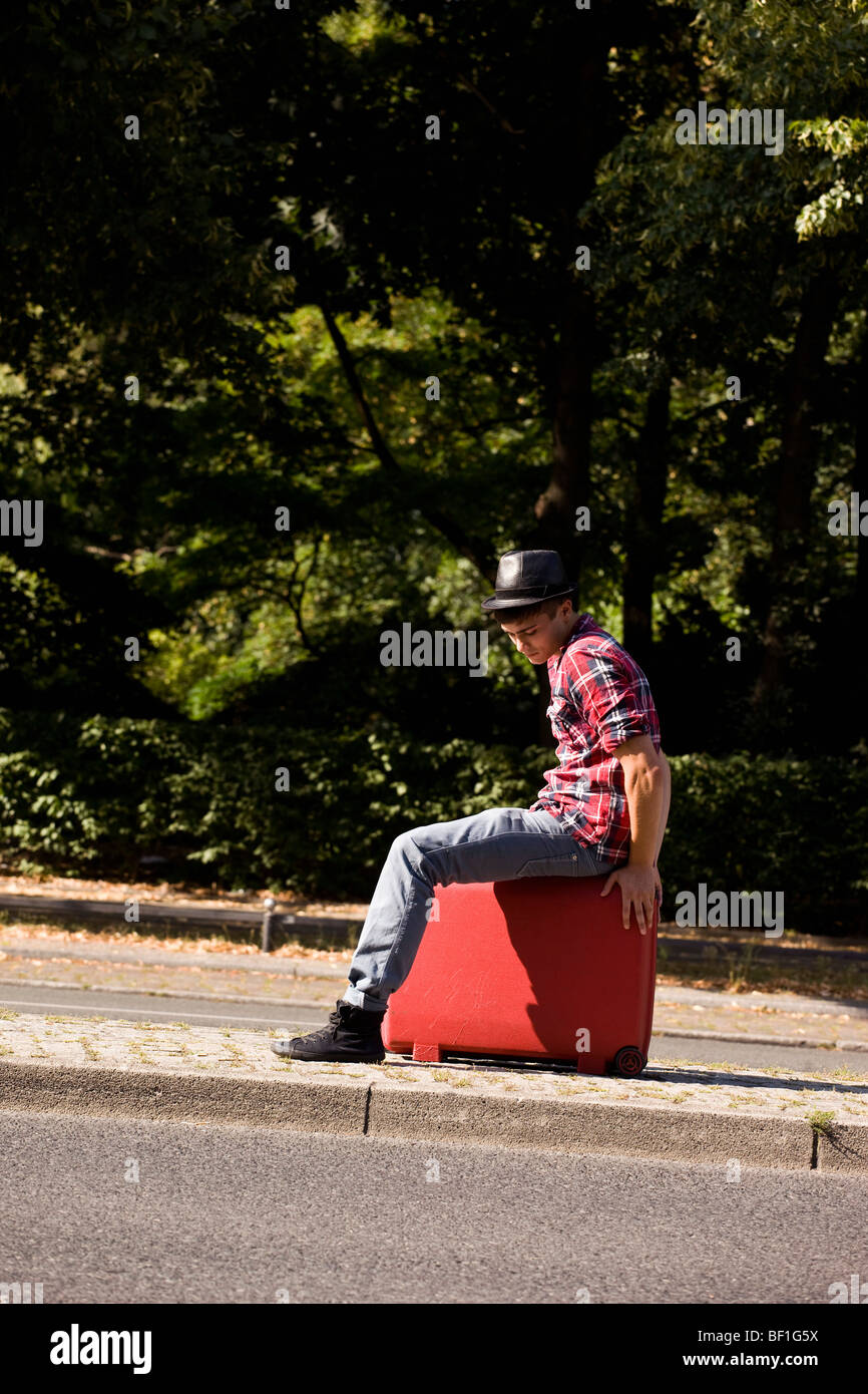 Ein junger Mann sitzt auf einem Koffer Stockfoto