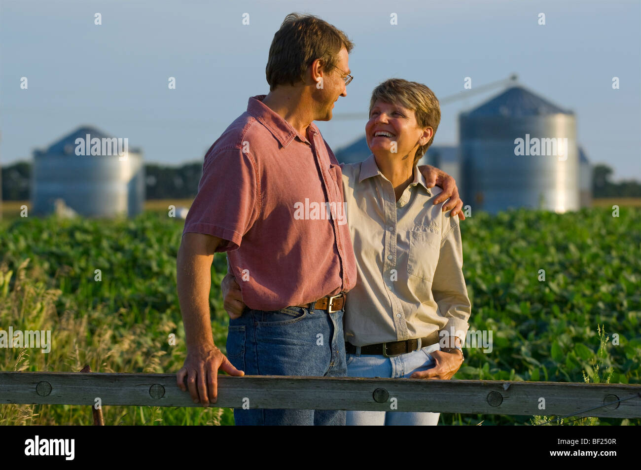 Mann und Frau Bauern in ihrem Soja-Bereich einige persönliche Momente miteinander teilen, mit Getreidesilos im Hintergrund / USA. Stockfoto
