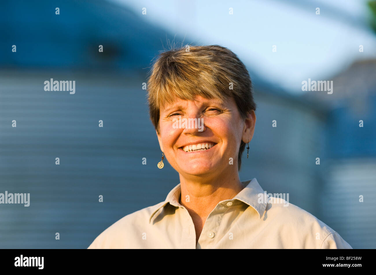 Landwirtschaft - Porträt einer lächelnden Bäuerin im Feld mit Getreide-Behälter im Hintergrund unscharf / Minnesota, USA. Stockfoto
