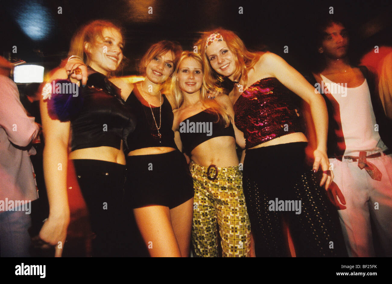Vier glückliche lächelnde Mädchen gekleidet in siebziger Jahre Kostüm, tanzen im Skandal Nachtclub. London, England Stockfoto