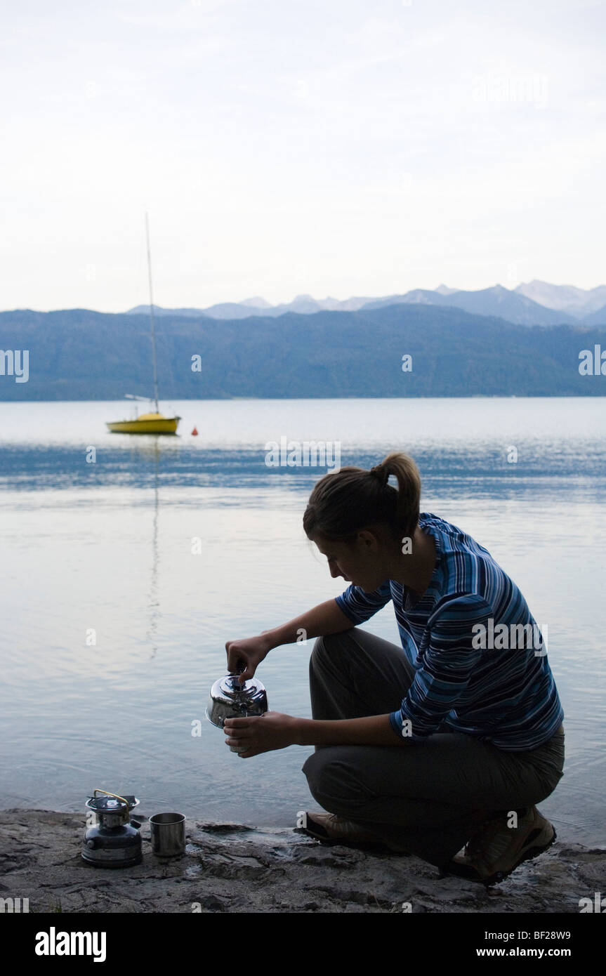 Eine junge Frau macht einen Drink auf einer Küche Herd am See Walchensee, Upper Bavaria, Bavaria, Germany Stockfoto