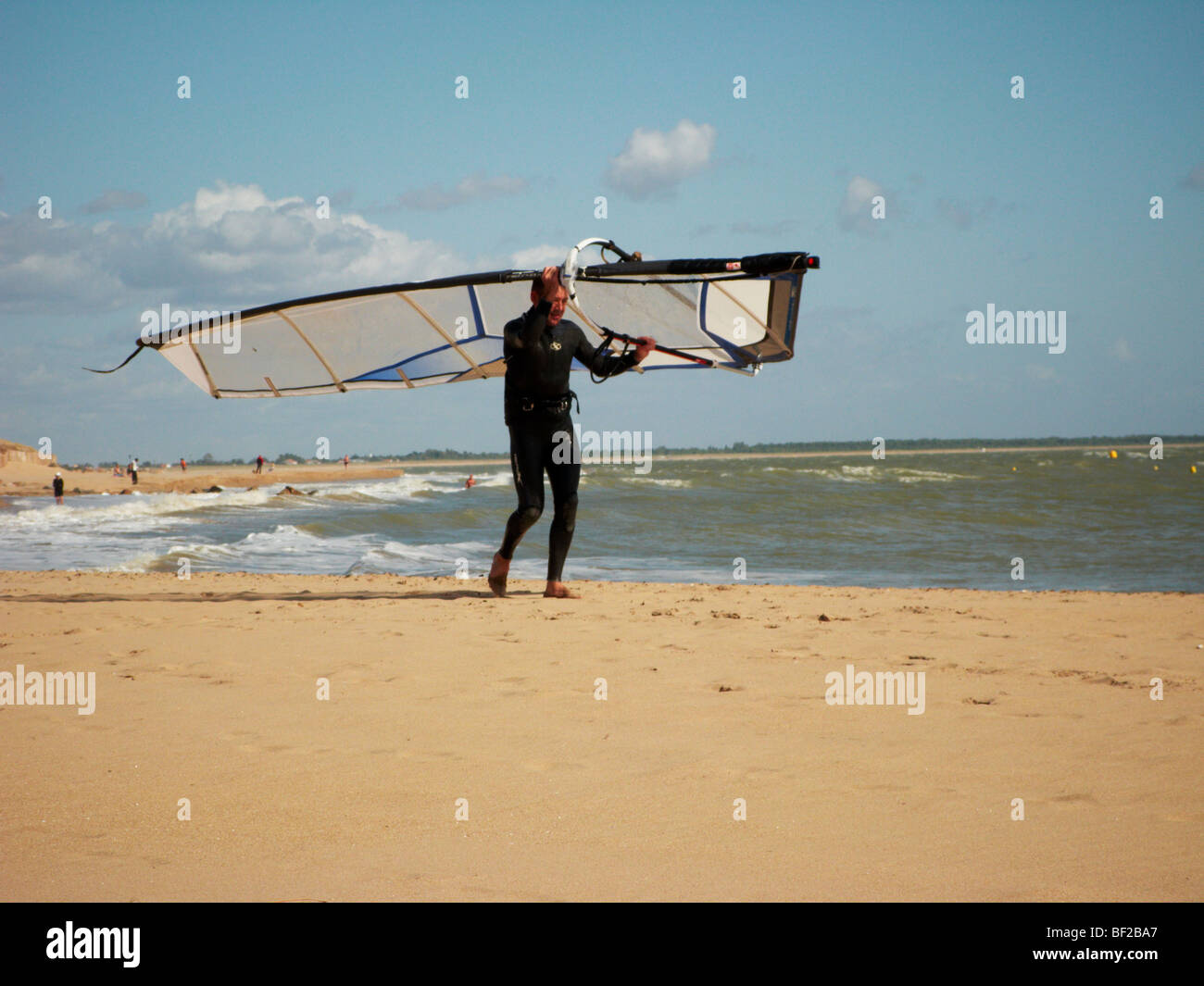 Ein Mann trägt seine Windsurfer am Strand entlang Stockfoto