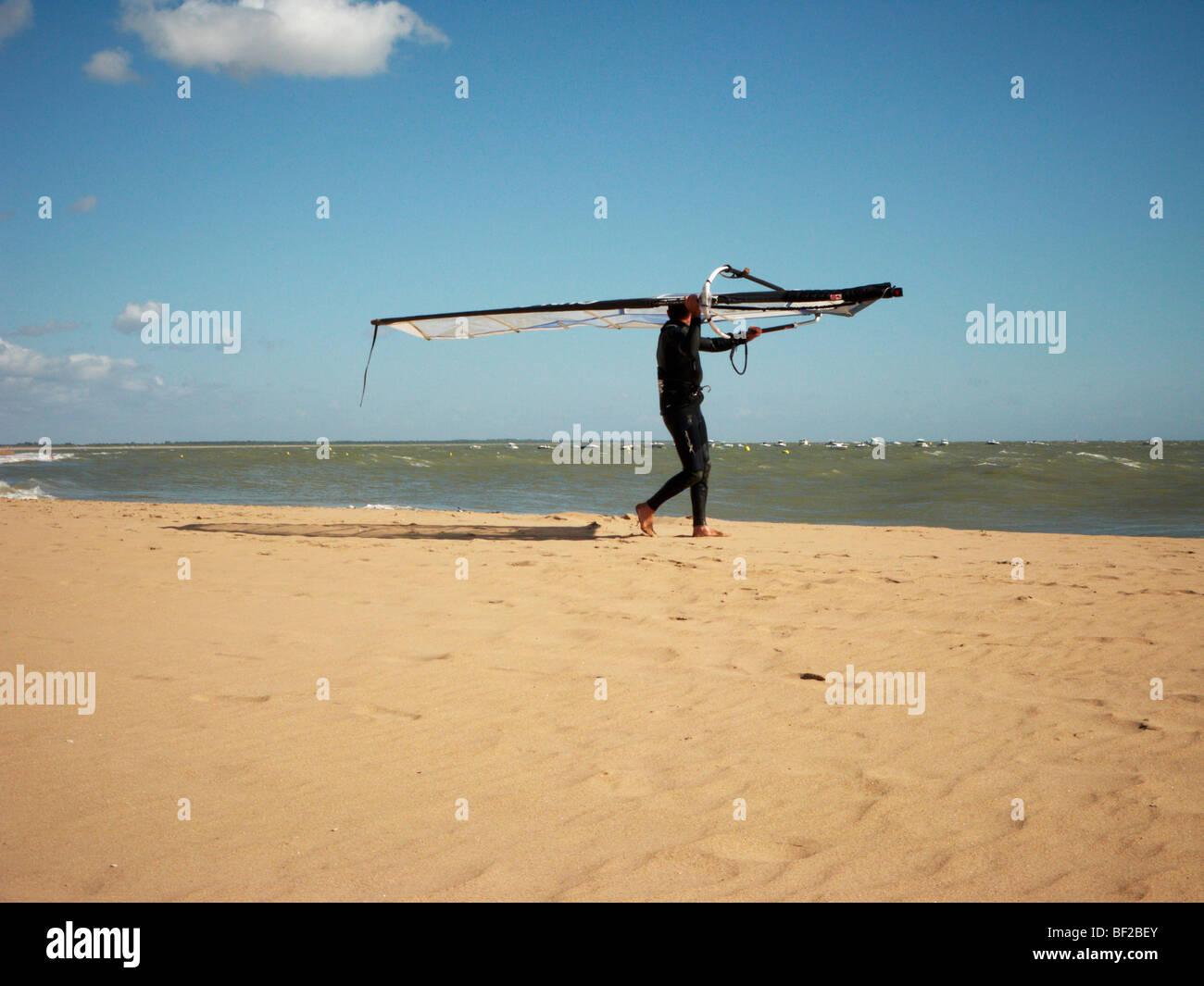 Ein Mann trägt seine Windsurfer am Strand entlang Stockfoto