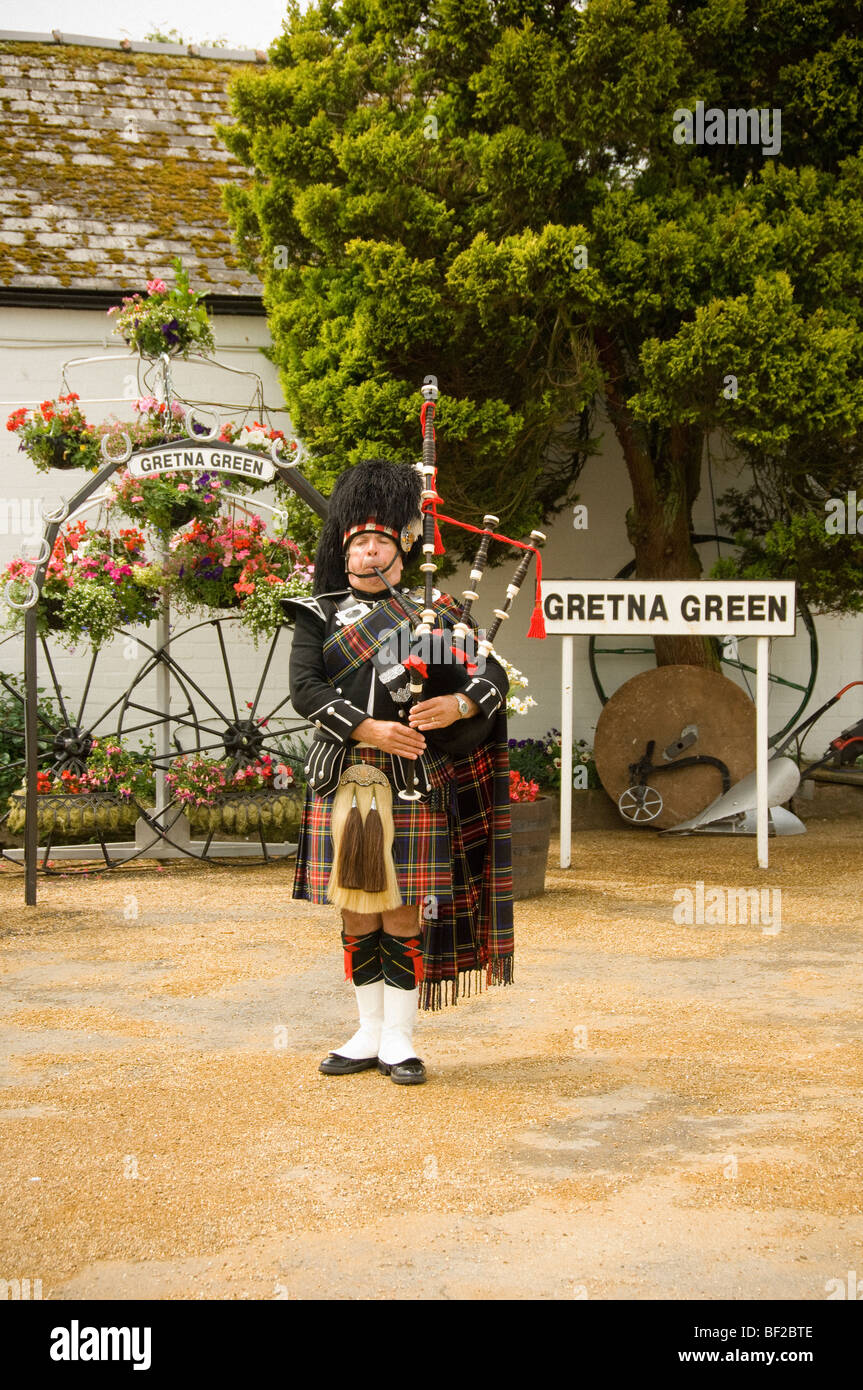 Kaukasischer schottischer Pfeifer, der vor dem Geschäft von Gretna Green Old Blacksmith, Schottland, Dudelsäcke spielt. VEREINIGTES KÖNIGREICH Stockfoto