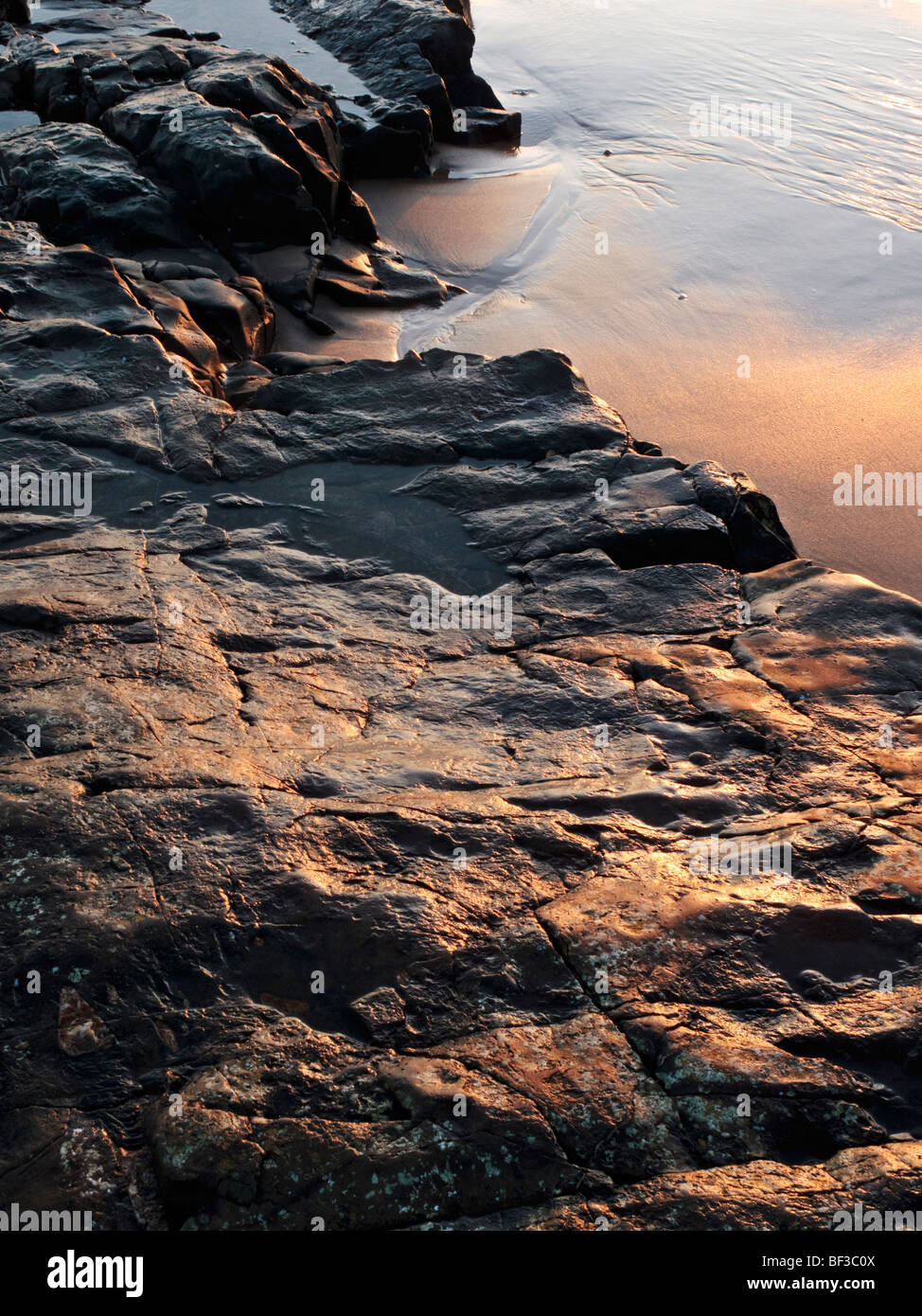 Die schwarzen Eruptivgestein der Northumbrian "Whin Sill" Bildung mit dem Licht der aufgehenden Sonne in der Nähe von Bamburgh Glühen Stockfoto
