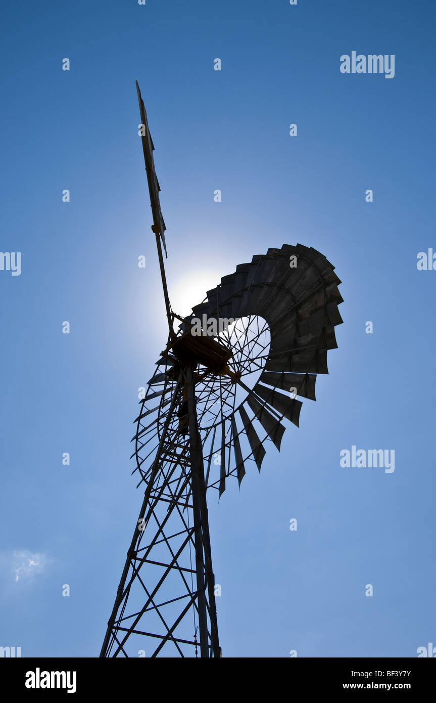 Eine alte Farm Windmühle mit der Sonne dahinter, vor blauem Himmel. Stockfoto