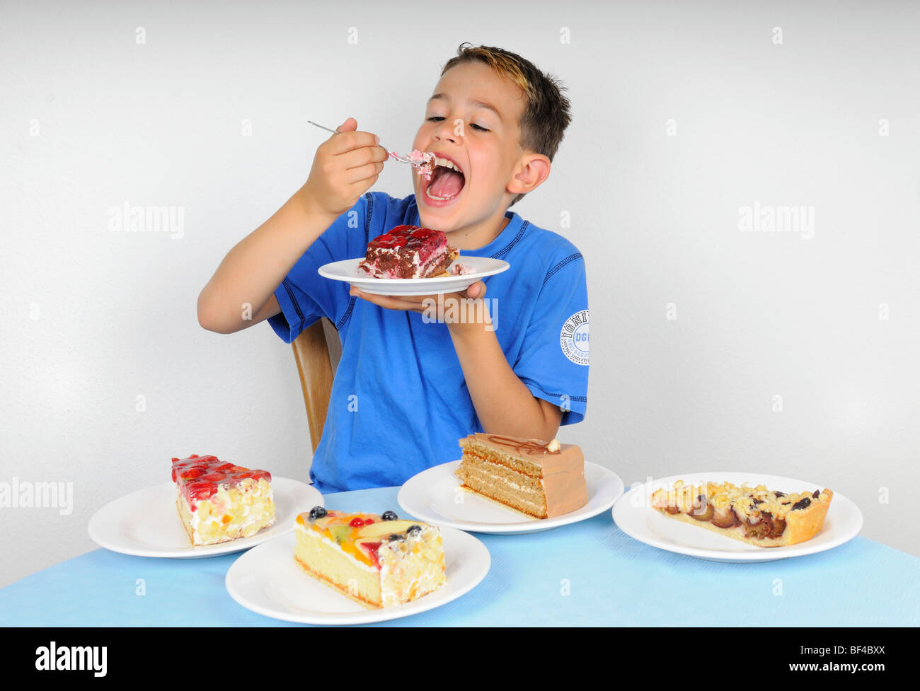 Junge, Kuchen essen, an einem Tisch mit vier Platten mit anderen Stücke des Kuchens Stockfoto