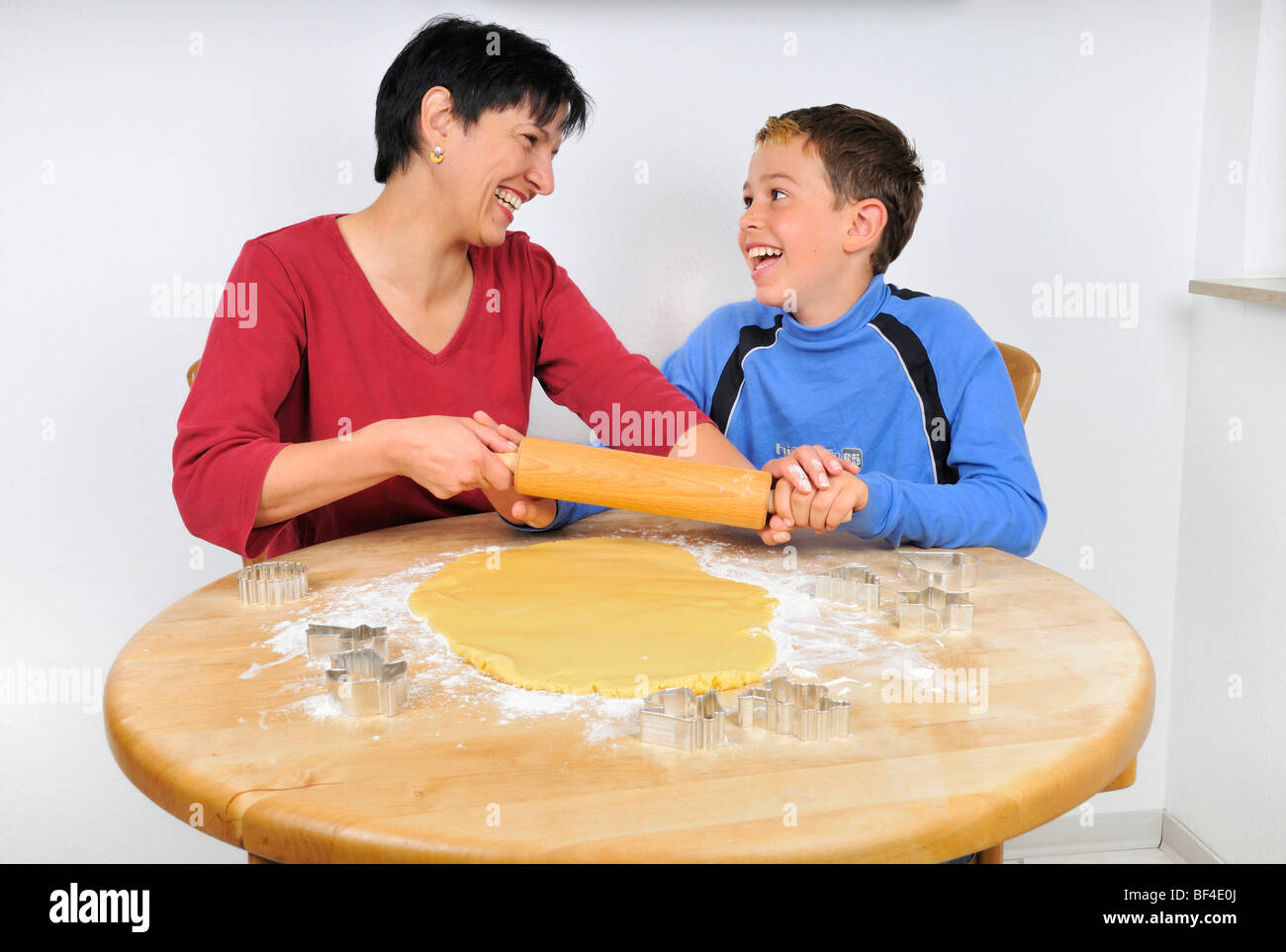 Weihnachtsbäckerei, Mutter und Sohn den Teig für Weihnachtsplätzchen mit einem Nudelholz ausrollen, liegen die Ausstechformen auf th Stockfoto