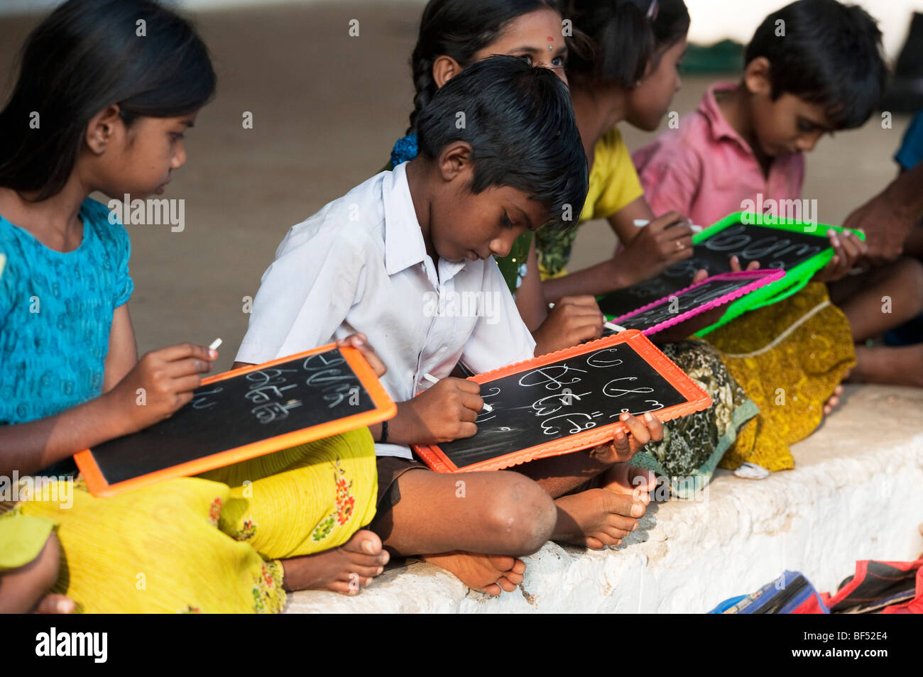Indian School Kinder sitzen außerhalb ihrer Schule schreiben auf der Schiefertafel. Andhra Pradesh, Indien. Selektive konzentrieren. Stockfoto