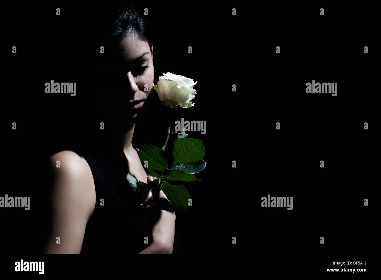 Junge dunkelhaarige Frau sucht traurig auf den Boden und hielt eine weiße Rose in der hand Stockfoto