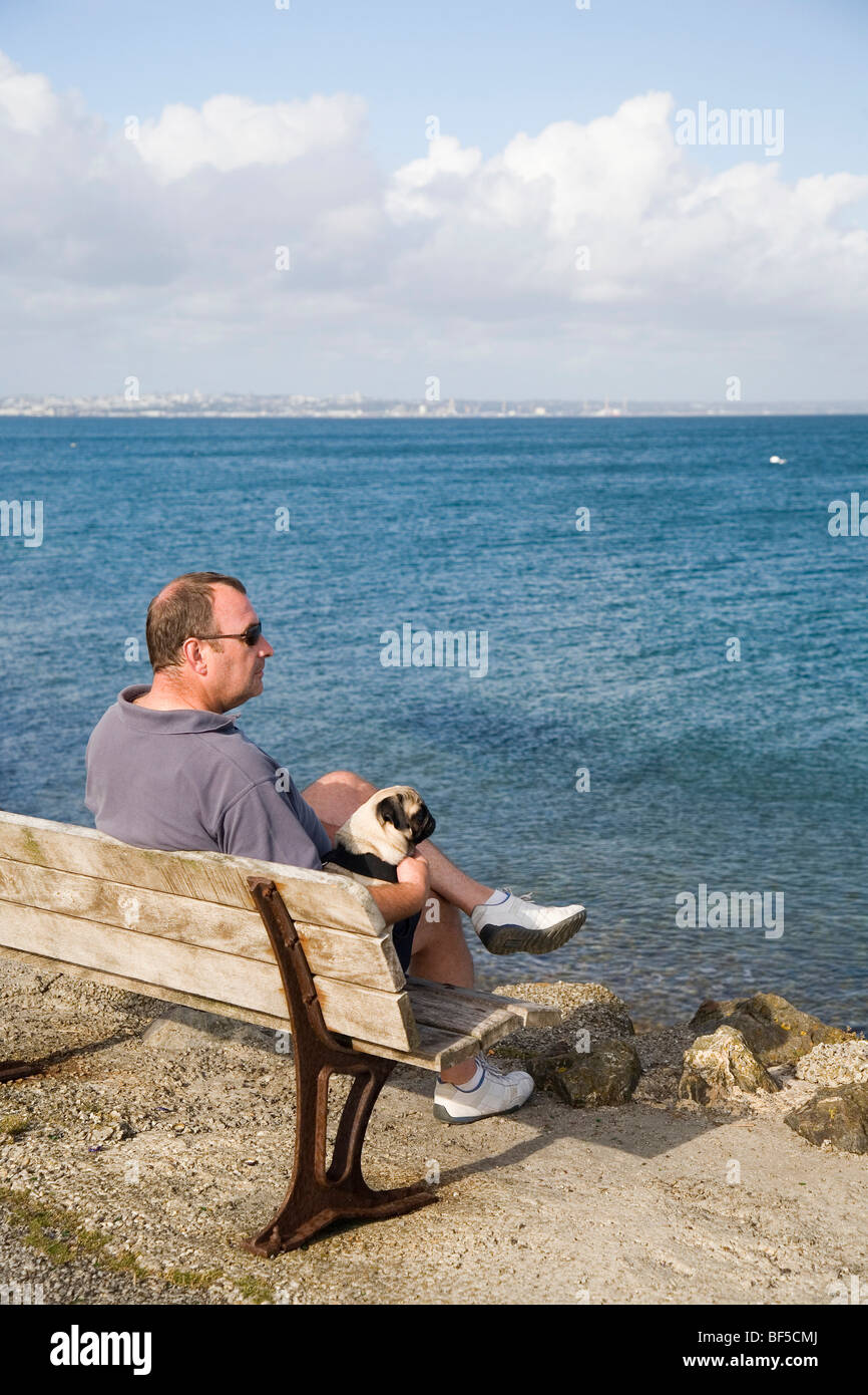 Ein Mann und sein Hund auf einer Bank am Meer sitzen und die Aussicht genießen Stockfoto