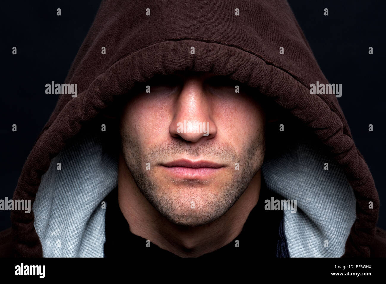 Eine böse aussehenden Mann trug ein Kapuze-Top mit seinen Augen verborgen vor einem schwarzen Hintergrund. Stockfoto
