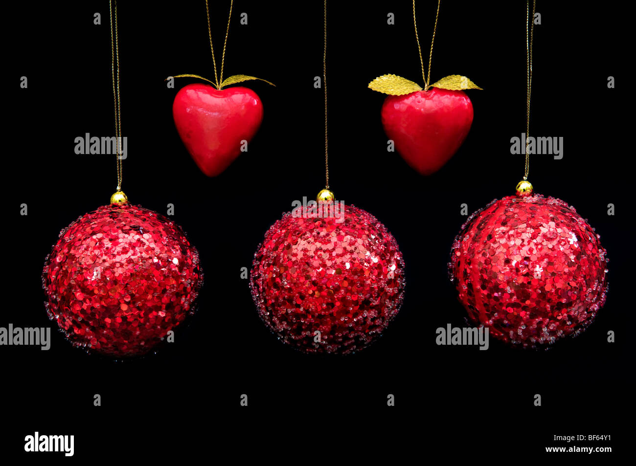 Fünf rote farbige dekorative Kugeln und Herzformen hängen mit Goldfäden vor schwarzem Hintergrund Stockfoto