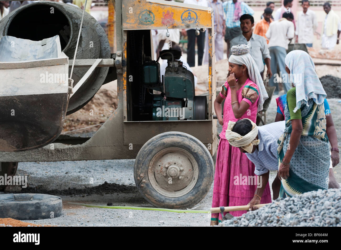 Indische Frauen neben einem großen Betonmischer, während auf den Straßen in Puttaparthi, Andhra Pradesh, Indien, stehen. Stockfoto