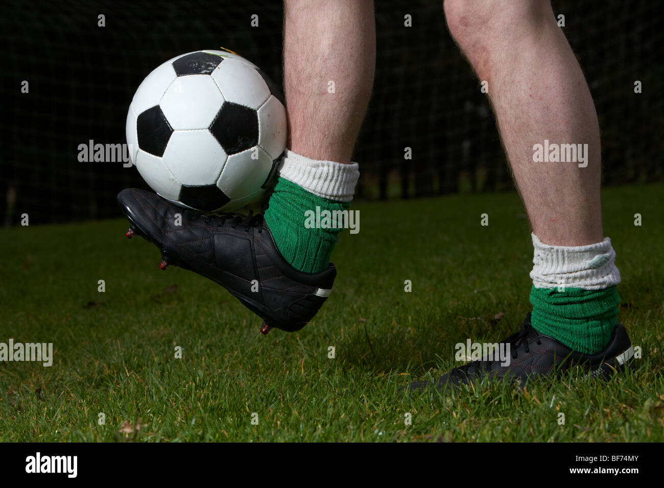 Fußball-Spieler balancieren Ball auf einem Fuß in Flutlicht Pitch allein Stockfoto