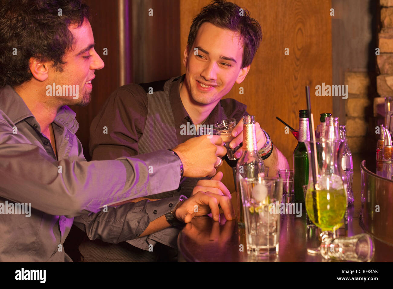 zwei Jungs in bar erhöhen ihre Gläser Stockfoto